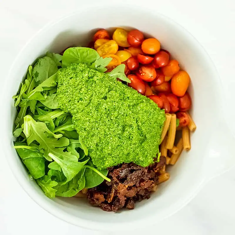 Large bowl filled with pasta, pesto, tomatoes, sundried tomatoes and spinach.