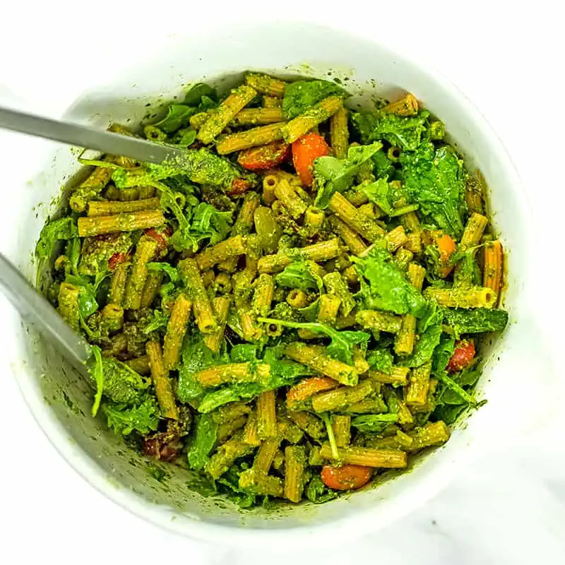 Pesto pasta salad ingredients after being tossed with tongs.