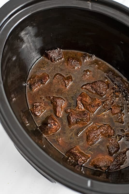 Slow cooker filled with cooked beef in balsamic sauce before shredding.