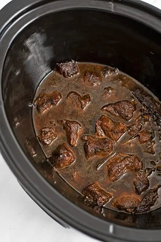 Slow cooker filled with cooked beef in balsamic sauce before shredding.