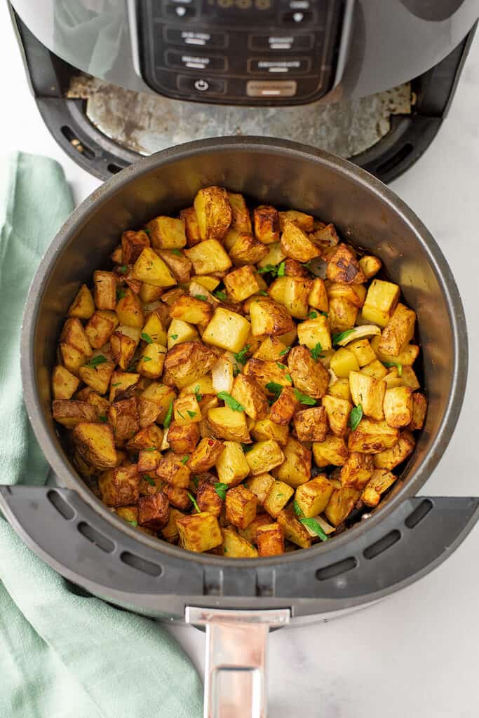 Roasted potatoes and onions in air fryer, green napkin on the side.