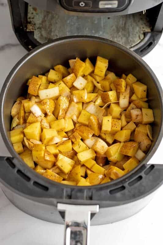 Air fryer basket filled with potatoes and onions before roasting.