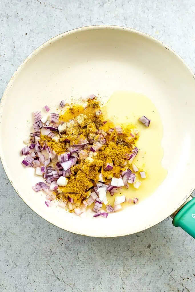 Oil, red onion and curry seasoning in skillet before cooking.