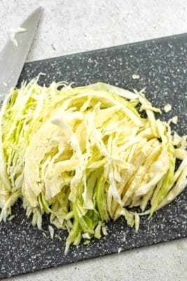 Thinly sliced cabbage on grey cutting board.