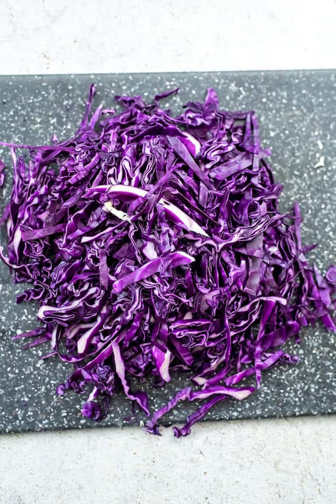 Thinly sliced purple cabbage on grey cutting board. 