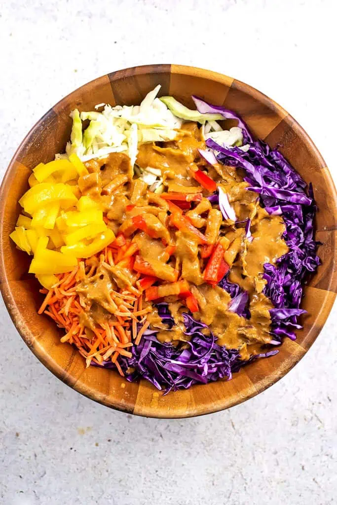 Peanut dressing poured over the veggies in wood bowl.