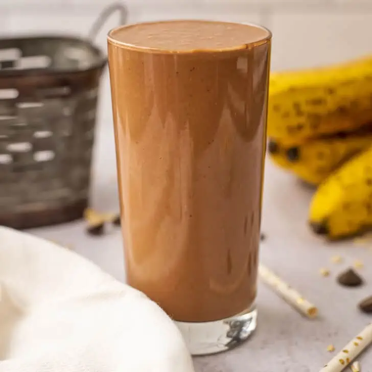 Banana chocolate oat smoothie in a tall glass with a white background.