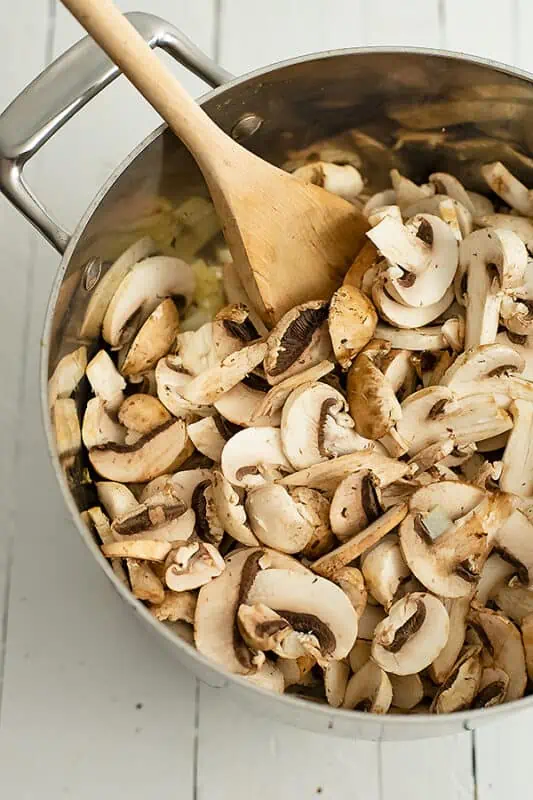 Sliced mushrooms being added to large pot with onions.