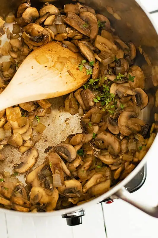 Wood spoon stirring fresh thyme into mushroom mixture.