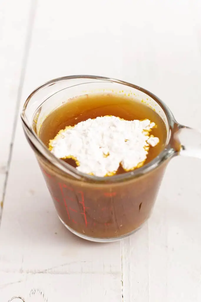 Arrowroot starch added to vegetable broth in glass measuring cup.