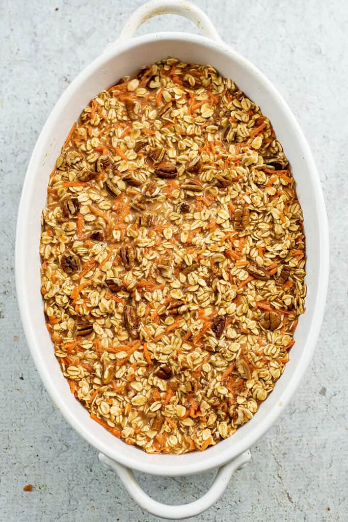 Chopped pecans spread on top of carrot cake oatmeal in casserole dish.