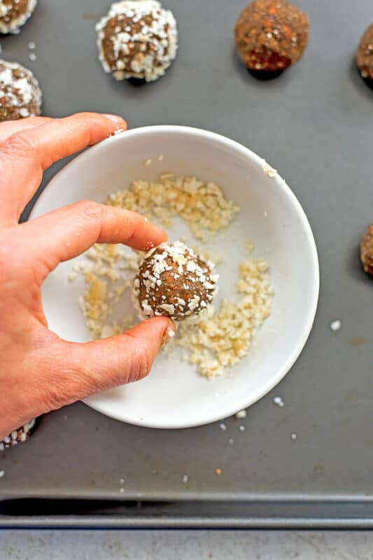 Hand rolling carrot cake protein ball in coconut flakes.