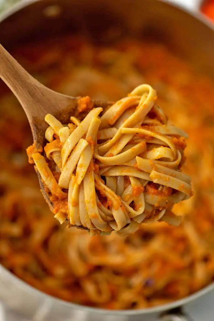 Wooden spoon holding pasta with carrot sauce.