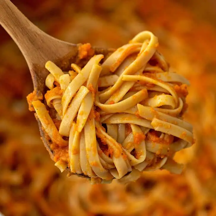 Wooden spoon holding pasta with carrot sauce.