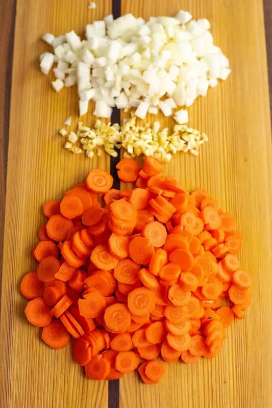 Chopped onion, garlic and sliced carrots on a wood cutting board.