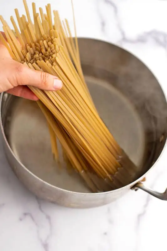 Hand dropping pasta in pot full of boiling water.