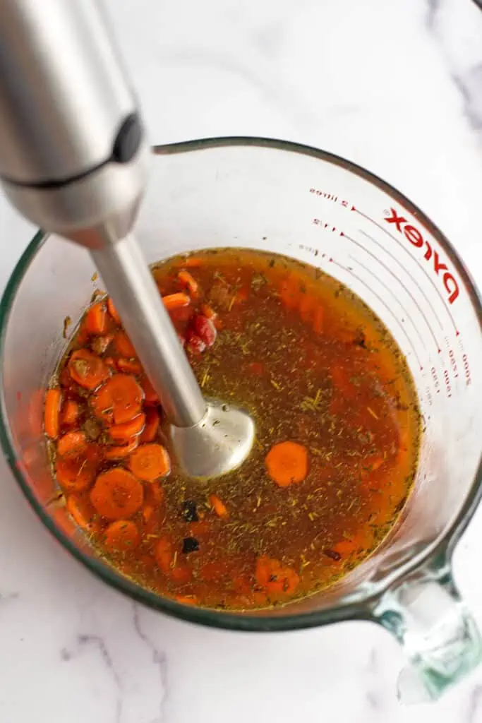 Immersion blender in glass bowl of carrots and vegetable broth.