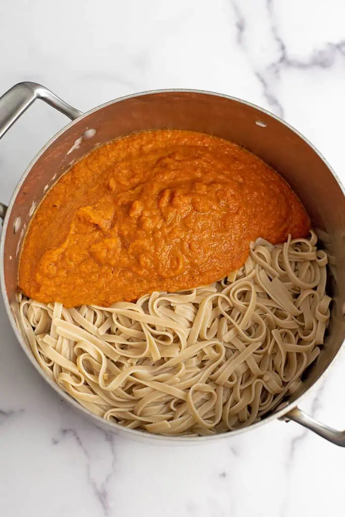 Carrot pasta sauce and cooked fettuccini in a large pot.