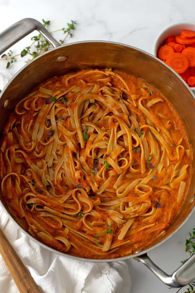 Carrot sauce pasta in a large silver pot with carrots in the background.