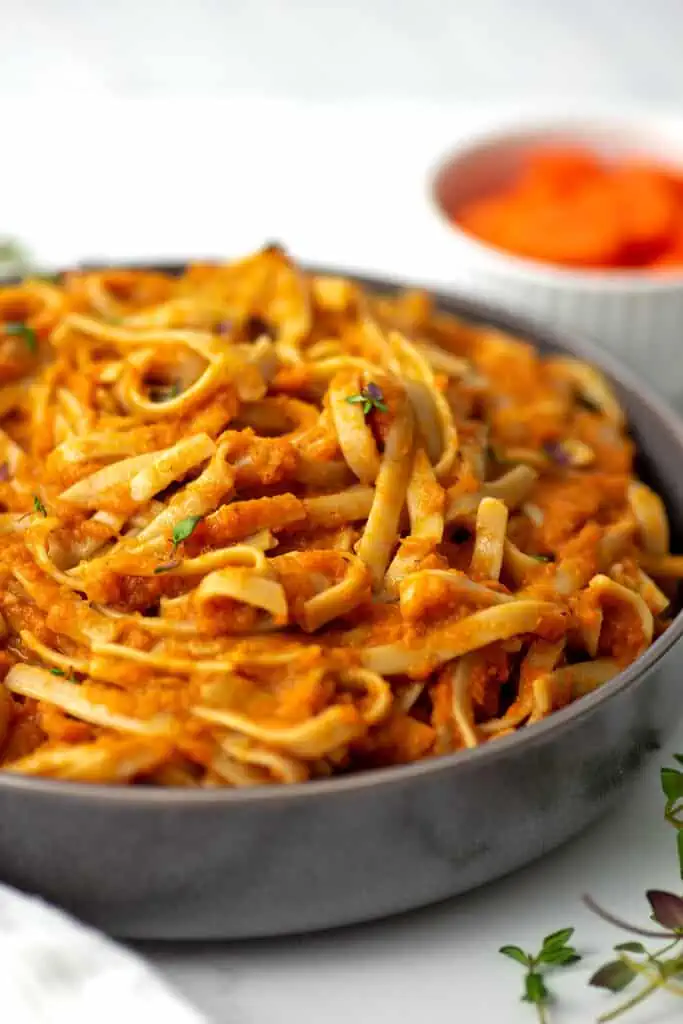 Carrot sauce pasta in a large grey bowl, carrots in the background.
