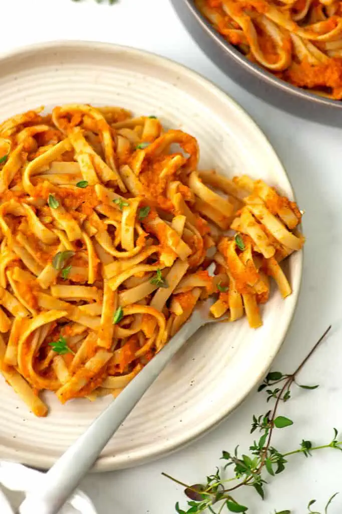 Carrot pasta twirled around a fork on a white plate.