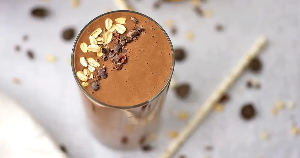 Chocolate banana oats smoothie with cacao nibs on top and scattered around the smoothie.