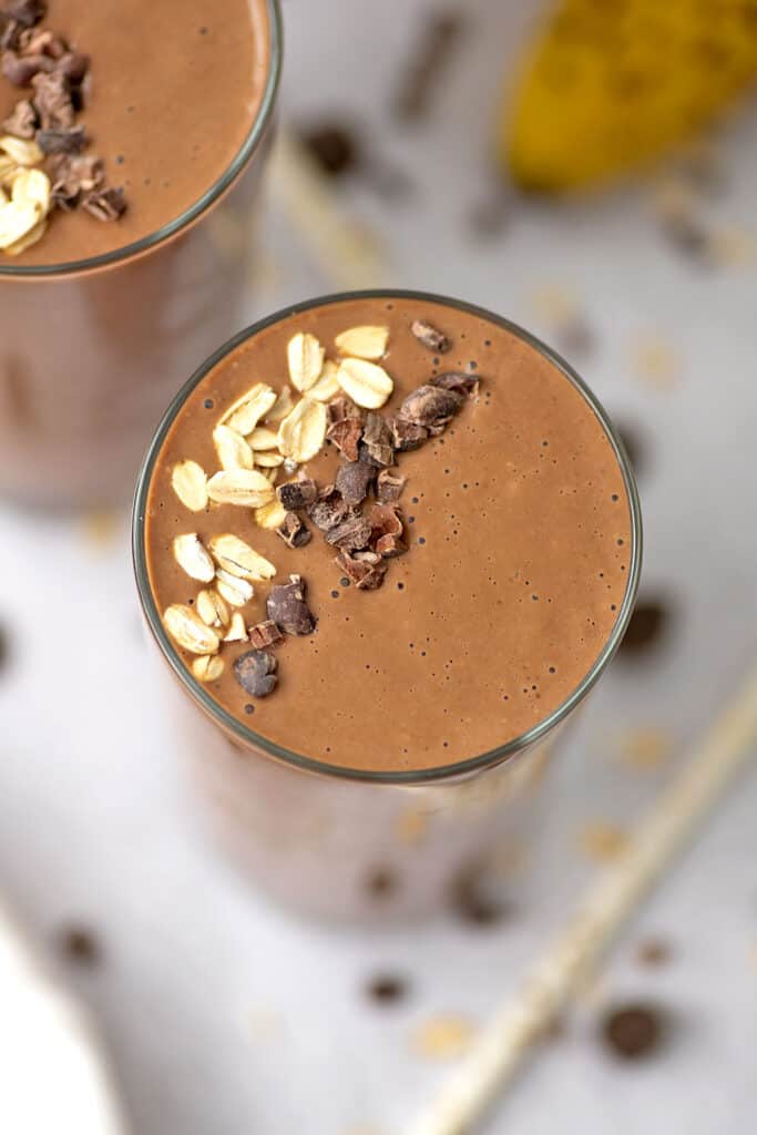 Chocolate oatmeal smoothie overhead view. The smoothie has oats and cacao nibs on top and is sitting on a white counter top.