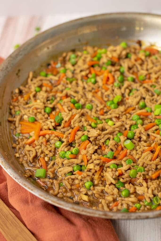 Asian ground chicken in skillet next to orange napkin.