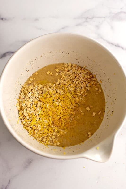 Rolled oats, lemon zest and baking powder added to ground flax mixture in bowl.