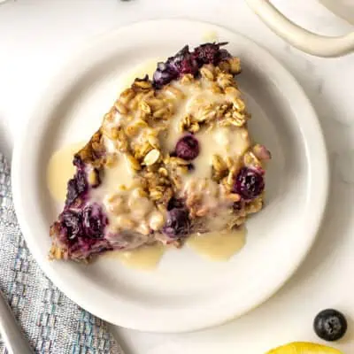 Blueberry lemon baked oats on a white plate, lemon yogurt drizzle on top.