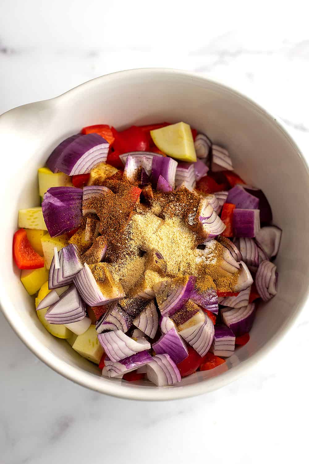 Spices on top of a bowl of chopped vegetables.