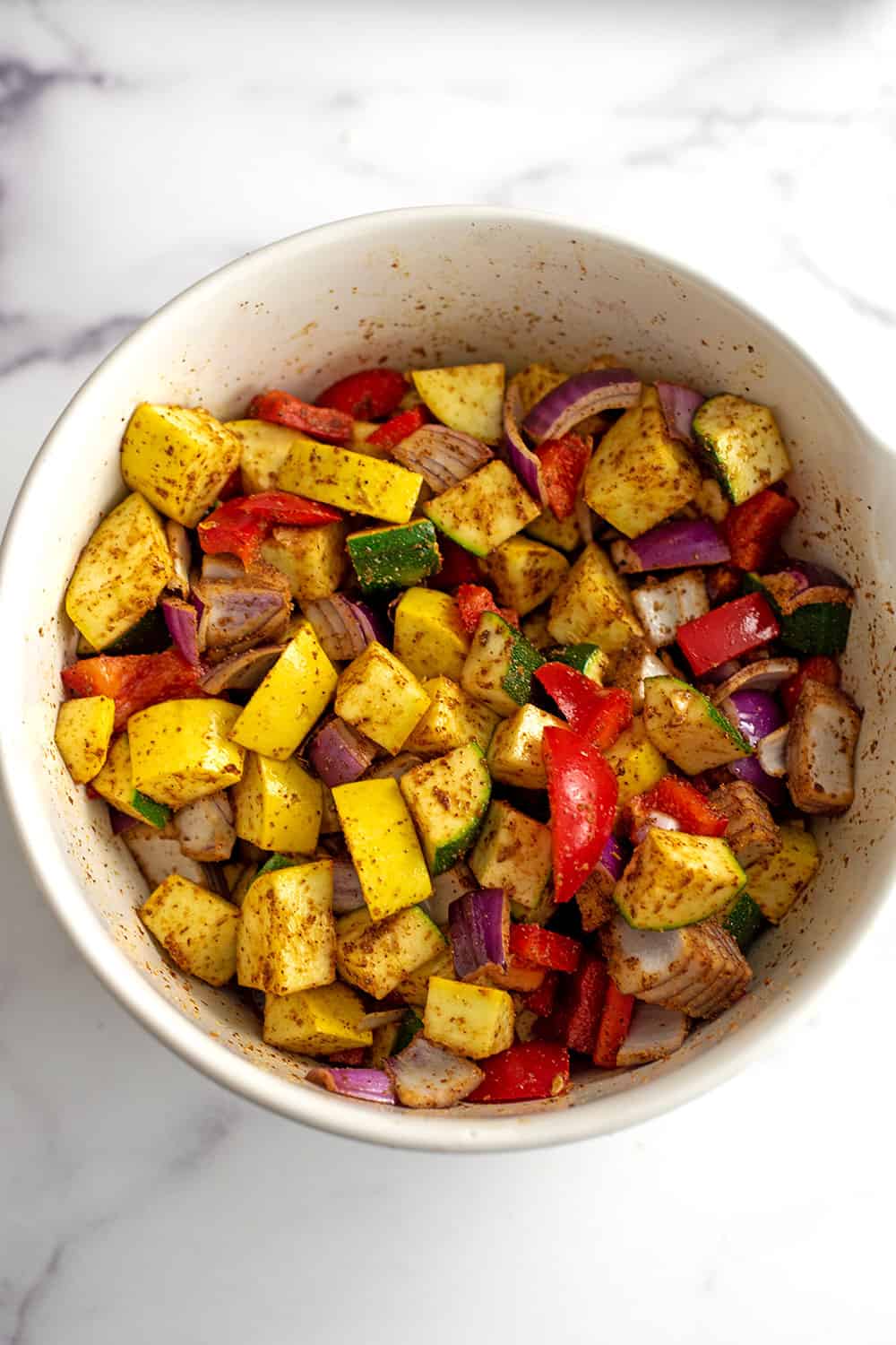 Chopped veggies in a white bowl coated in spices.
