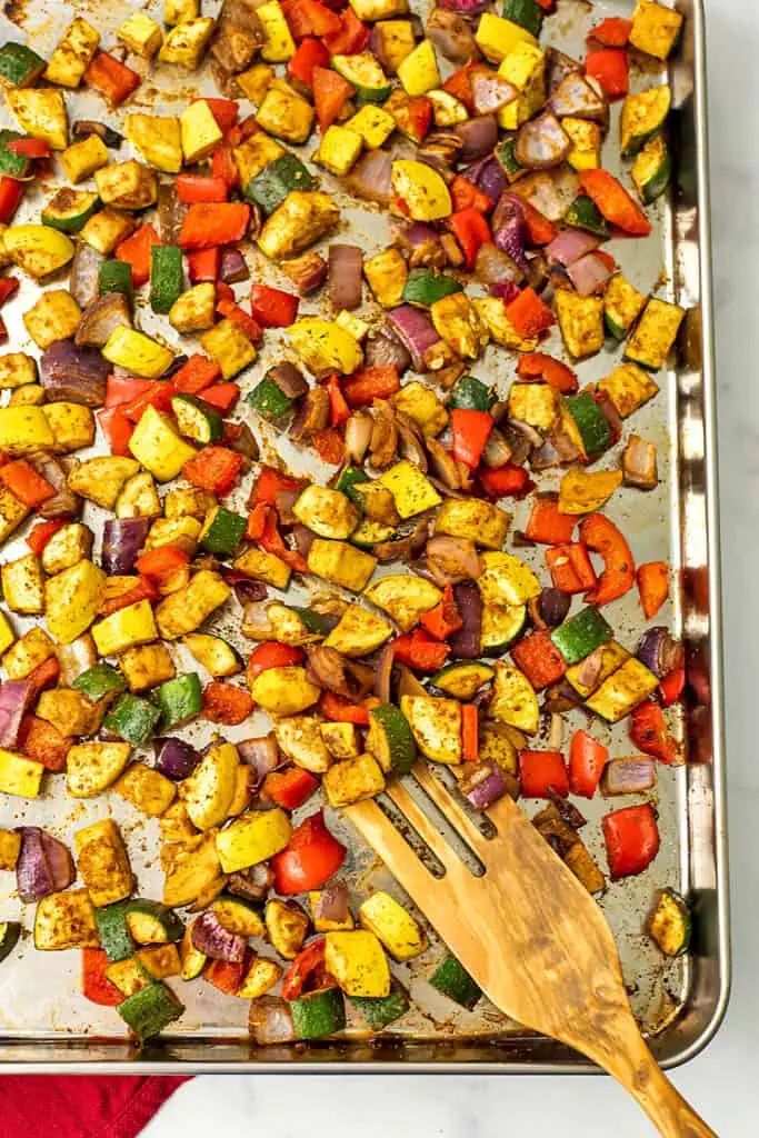 Mexican roasted vegetables on a silver sheet pan with a wood spatula.