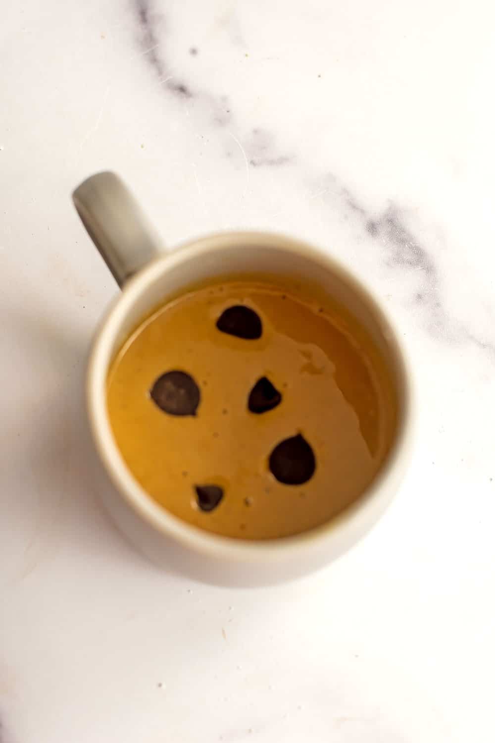 Chocolate chips added to oat flour batter in mug.