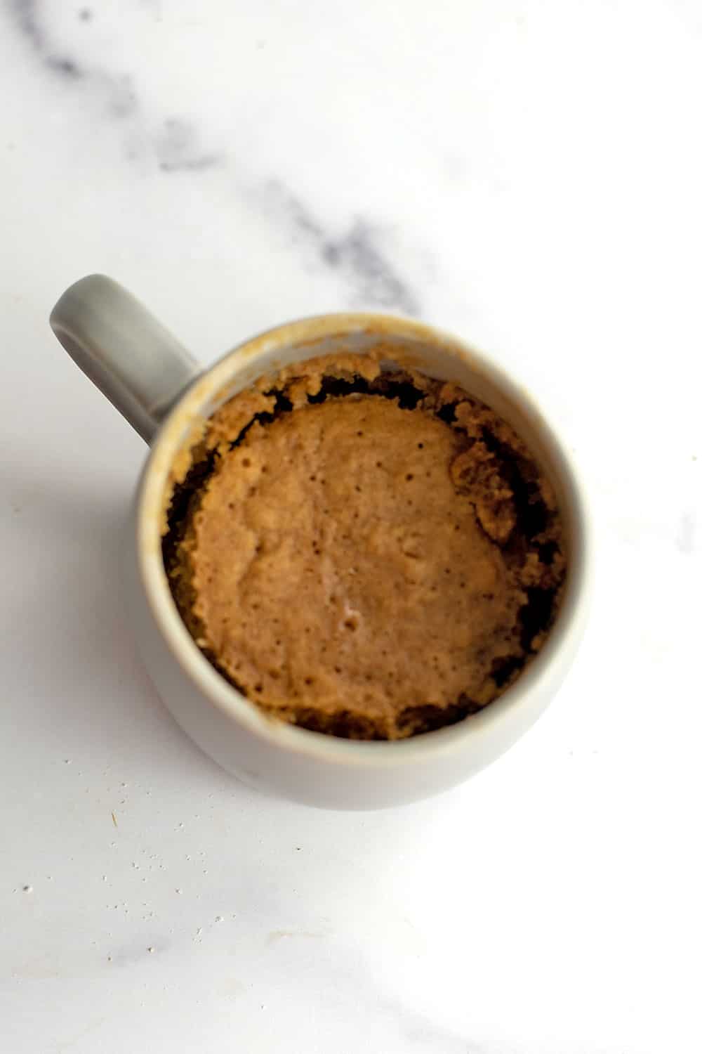 Oat mug cake after cooking on a marble countertop.