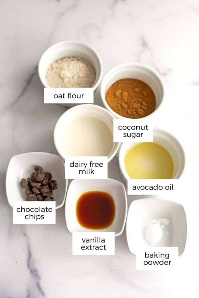 Ingredients to make oat mug cake in ramekins on marble countertop.