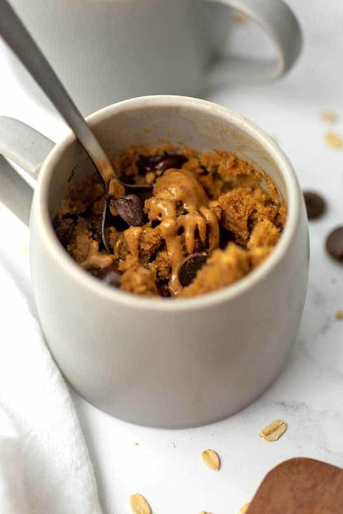 Mug full of oat flour cake with almond butter drizzled on top, spoon in mug.