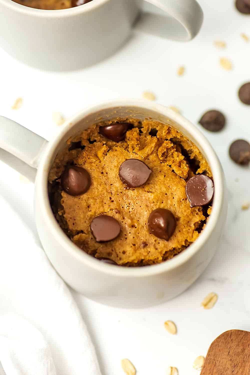 Grey mug filled with oat flour mug cake, chocolate chips on the side.