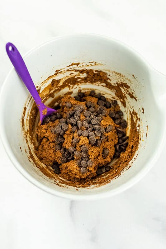 Chocolate chips added to pumpkin batter in white bowl.