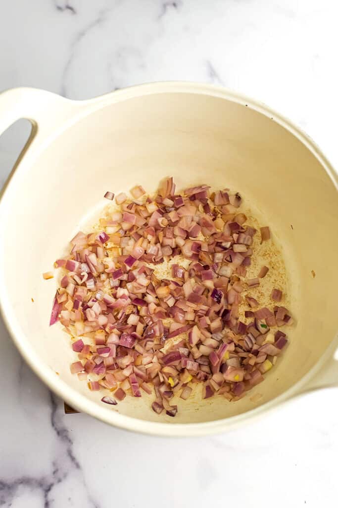 Sauteed red onions in a white pot.