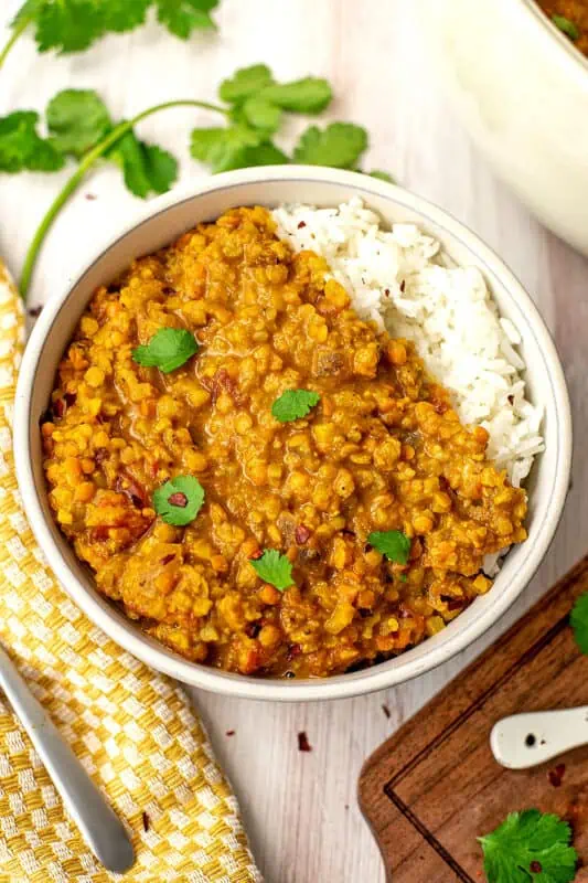 Cauliflower red lentil curry in a bowl with jasmine rice with yellow napkin on the side.