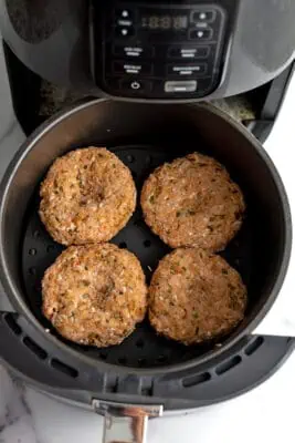 Raw chicken burgers in air fryer basket.