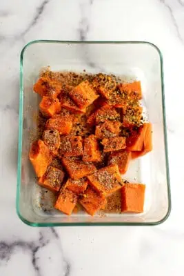Spices on salmon cubes in glass container.