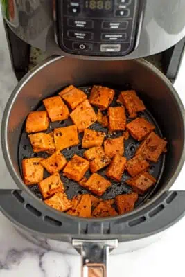 Raw salmon bites with spices in air fryer basket.