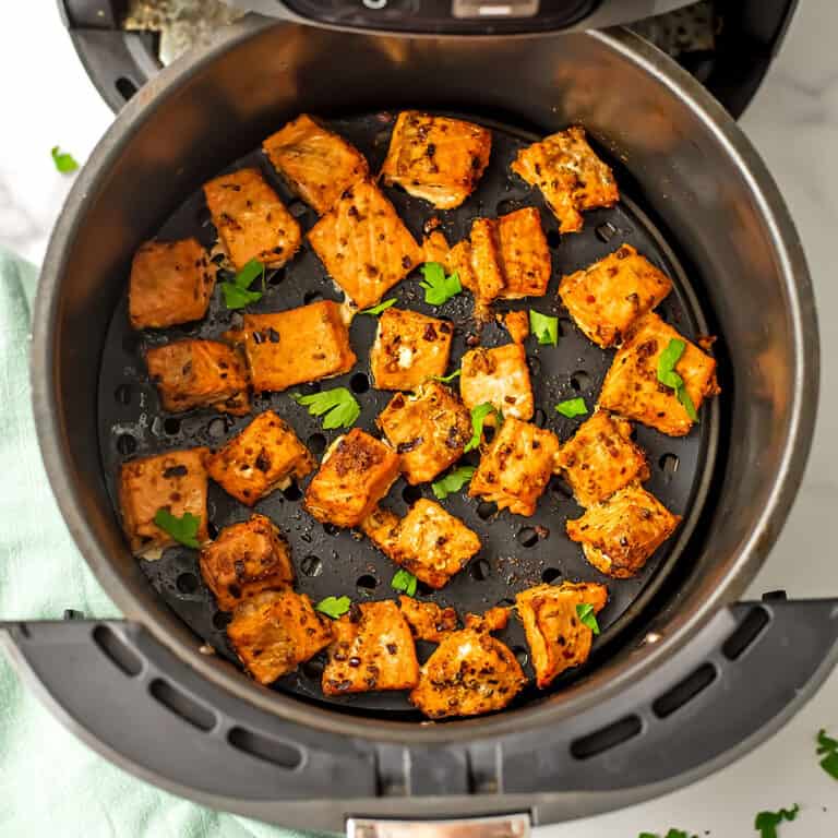 Salmon bites in air fryer basket with green napkin on the side.
