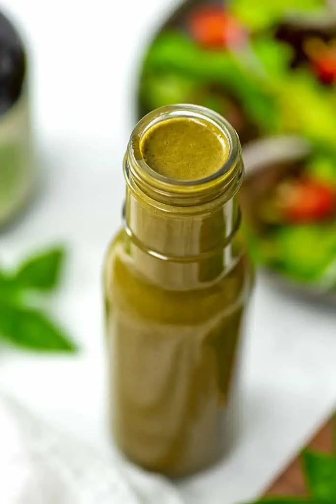 Basil balsamic vinaigrette in a glass bowl with salad in the background.