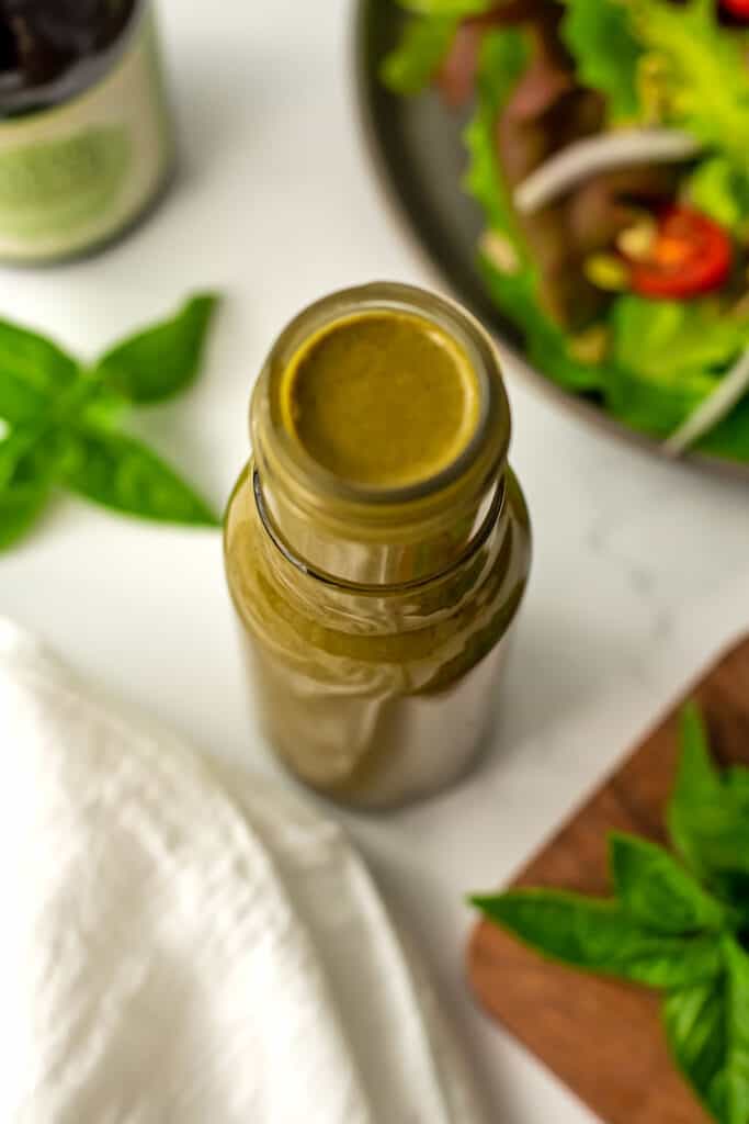 Basil balsamic vinaigrette in a glass bottle with basil leaves in backgroudn.