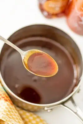 Spoonful of sticky sriracha honey sauce over a pot of sauce.