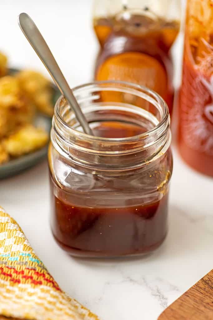 Glass jar of honey sriracha sauce with a spoon resting in the jar.