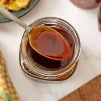 Spoonful of sriracha honey over a glass jar filled with sriracha honey sauce.